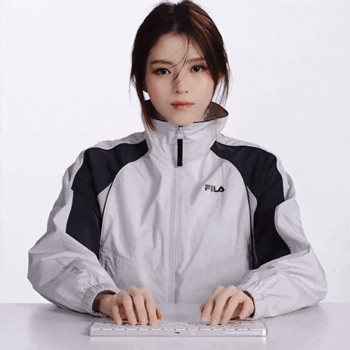 a woman in a fila jacket is typing on a computer keyboard