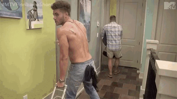 a shirtless man is holding a ladder in a hallway while another man stands behind him .
