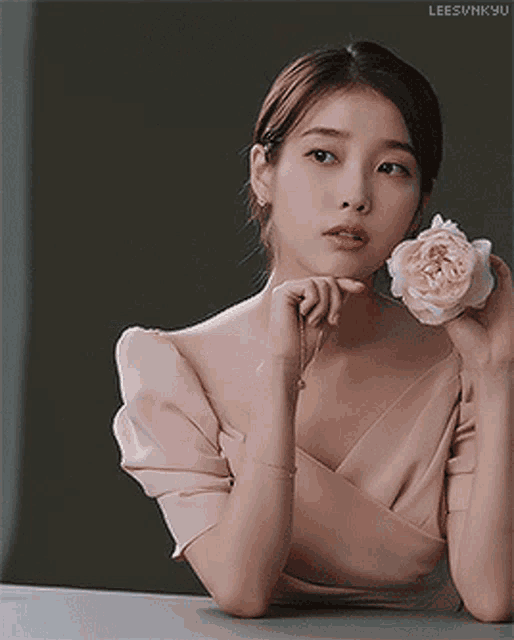 a woman in a pink dress is sitting at a table holding a rose .