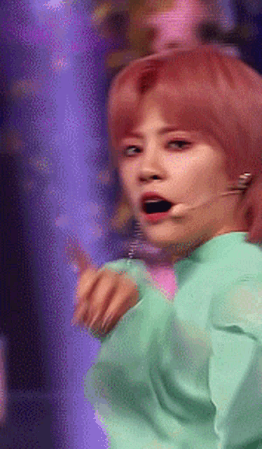 a woman with pink hair and a green shirt is singing into a microphone .