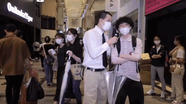 a man wearing a mask stands in front of a sign that says onitsuka tiger on it