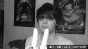 a black and white photo of a shirtless man holding two bananas in front of a wall with posters on it .