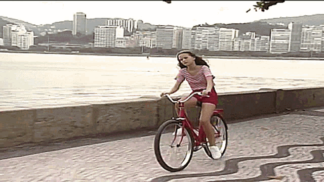 a woman is riding a red bicycle on a sidewalk near the water
