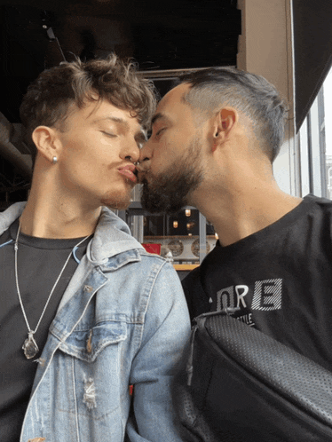 a man wearing a black t-shirt that says ore kisses another man on the cheek