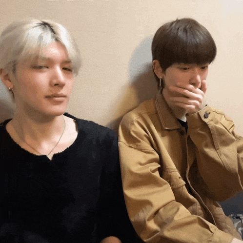 two young men are sitting next to each other and one is covering his mouth