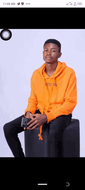 a young man in an orange hoodie is sitting on a black ottoman