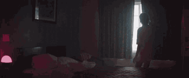 a woman in a white shirt stands in front of a window in a dark room