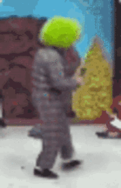 a clown with a green wig on his head is dancing on a stage .