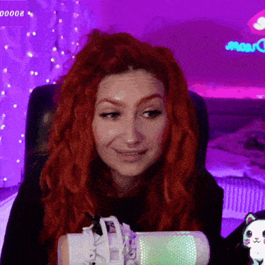 a woman with red hair is sitting in front of a microphone with a purple background and a purple sign that says 00000