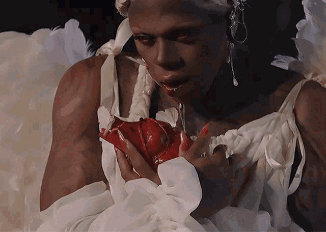 a woman in a white dress with angel wings holds a red rose in her hands