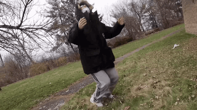 a person wearing a mask and a black jacket is dancing in the grass