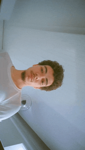 a man with curly hair is standing in front of a white wall