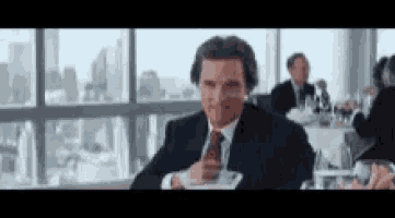 a man in a suit and tie is sitting at a table in front of a large window .