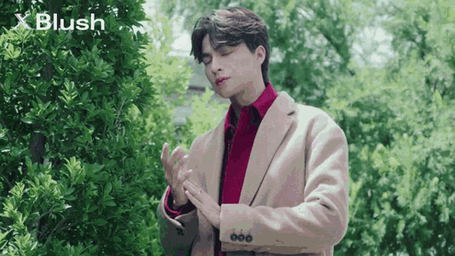 a man in a tan coat and red shirt is standing in front of a tree with x blush written on the bottom