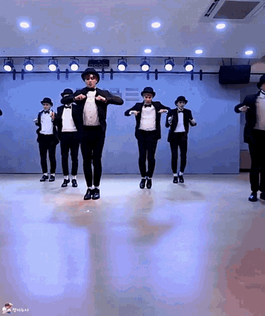 a group of men in tuxedos and hats are dancing in a room