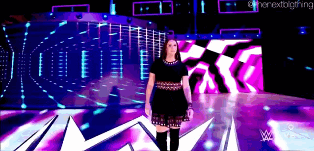 a woman in a black dress is standing on a stage with a purple and blue background ..