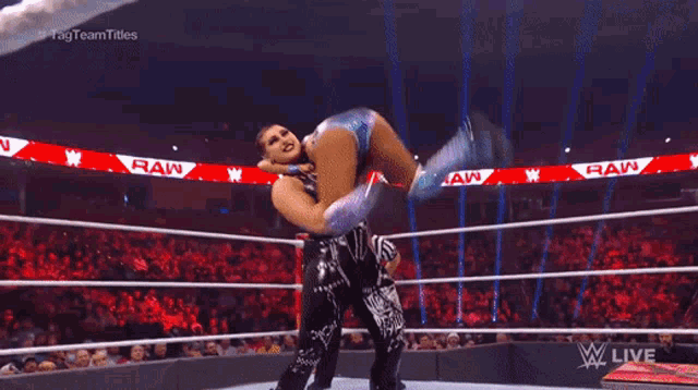 a female wrestler is doing a handstand in front of a sign that says raw live