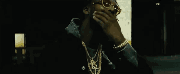 a man wearing sunglasses and a necklace is covering his mouth .