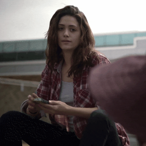 a woman in a plaid shirt is sitting on the ground looking at her phone