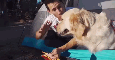 a man is feeding a dog a slice of pizza