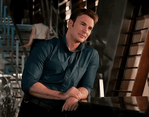a man in a blue shirt is leaning on a table with his hands on his hips .