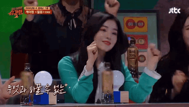 a woman in a green jacket is sitting at a table with a bottle of jtbc on it