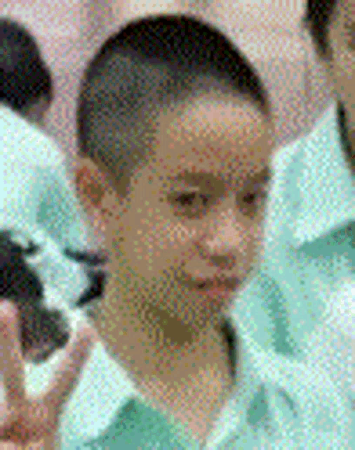 a boy with a shaved head is wearing a green shirt and giving a thumbs up sign .