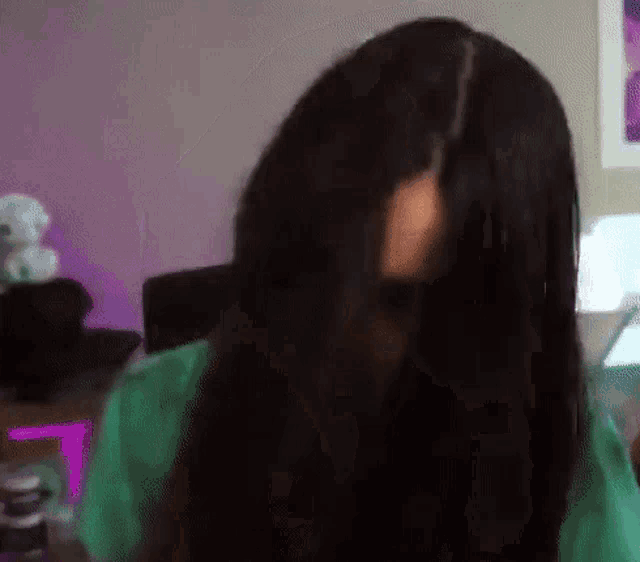 a woman with long black hair is sitting in front of a computer and looking at the camera .