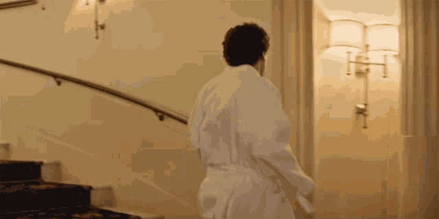 a man in a bathrobe walks down stairs