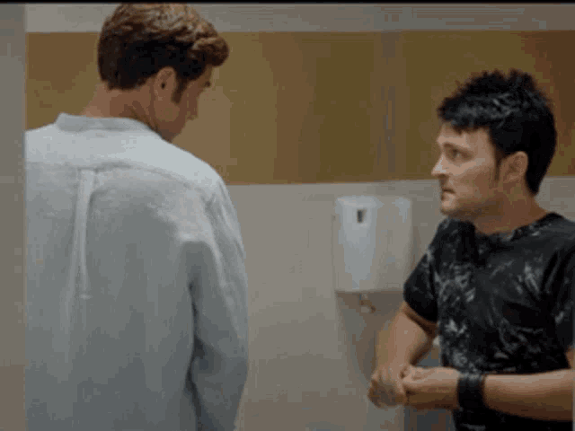 two men standing next to each other in a public bathroom