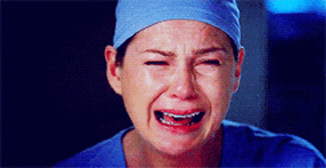 a woman wearing a surgical cap and scrubs is crying with her eyes closed