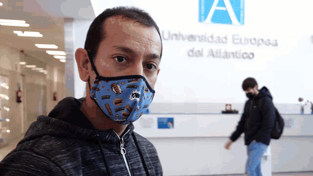 a man wearing a face mask is standing in front of a sign that says universidad europea del atlantico