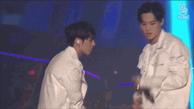 two men are standing next to each other on a stage and one of them is giving a peace sign