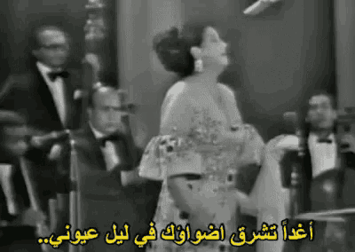 a black and white photo of a woman singing in front of a microphone with arabic writing on the bottom