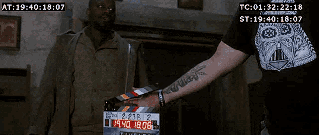 a man with a tattoo on his arm is holding a clapper board with the number 2036 2 on it