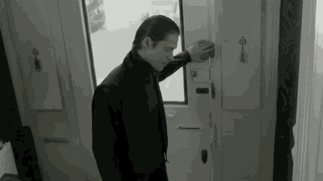 a man in a black jacket and blue gloves is opening a white door