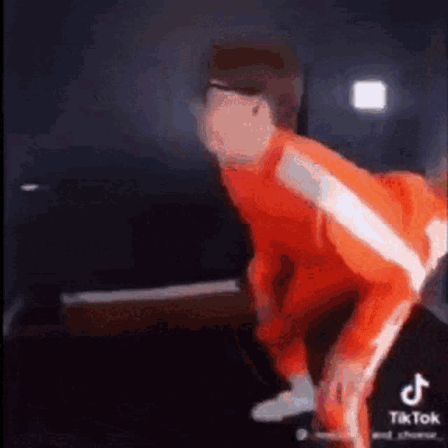 a man in an orange jumpsuit is dancing in a room .