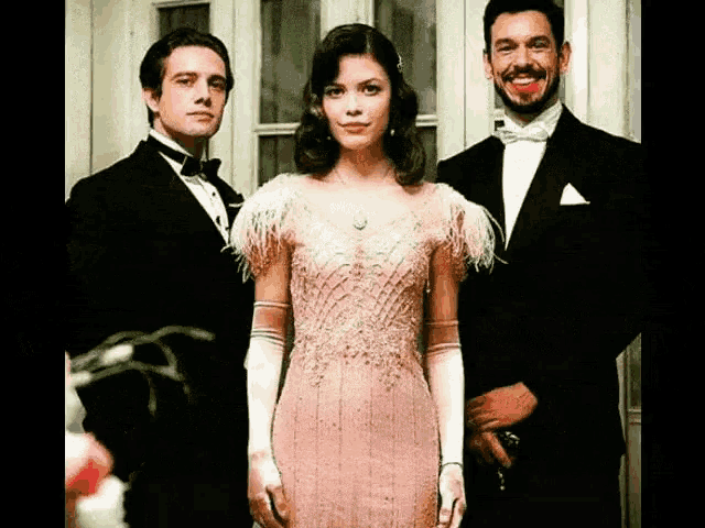 a woman in a pink dress is standing between two men in suits