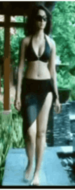 a woman in a bikini and skirt is walking on a sidewalk .