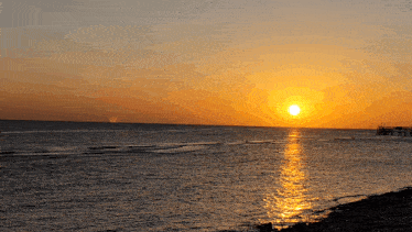 the sun is setting over the ocean with a pier in the background