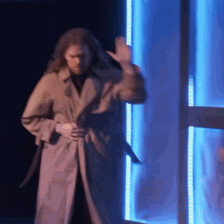 a man in a trench coat is waving his hand