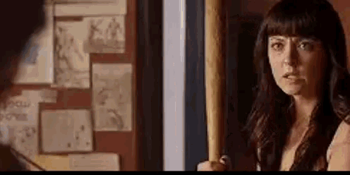 a woman is holding a baseball bat and looking at a man in a room .