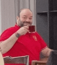 a man in a red shirt is drinking a cup of tea .