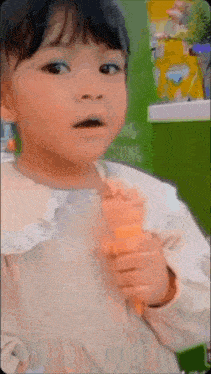a little girl is eating an ice cream cone and making a funny face .