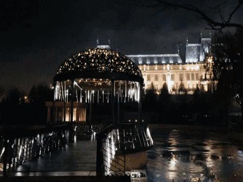 a gazebo is lit up at night with a building in the background