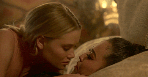two women are kissing on a bed and one of them is wearing earrings