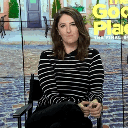 a woman in a black and white striped shirt is sitting in front of a screen that says the good place