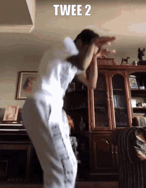 a man in a white shirt is dancing in a living room with twee 2 written above him