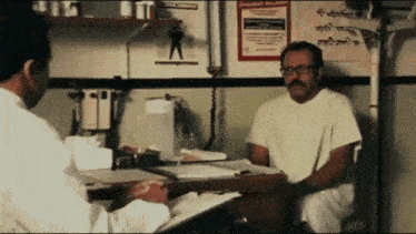 a doctor is talking to a patient who is sitting at a desk with a clipboard