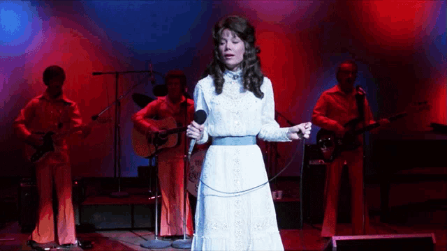 a woman in a white dress is singing into a microphone on stage